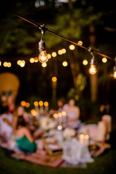 an outdoor dinner with lights strung over the table and people sitting around it at night