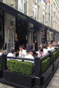 people sitting at tables in front of a restaurant on a city street lined with tall buildings