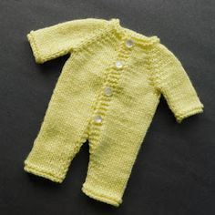 a yellow knitted baby's sweater laying on top of a black surface with buttons