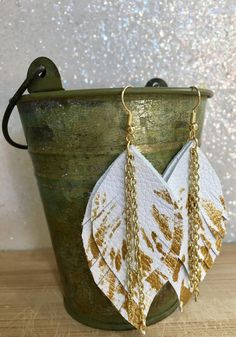 two white and gold leaf shaped earrings with chains hanging from the side on a bucket