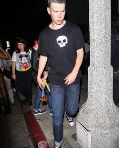 a young man standing on the sidewalk with his hands in his pockets and wearing black converse shoes