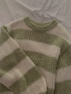 a green and white striped sweater laying on top of a bed next to a pillow