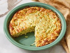 a cheesy quiche in a green dish with a slice missing from it