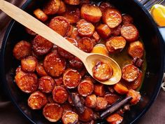 a skillet filled with cooked carrots next to an orange slice and wooden spoon