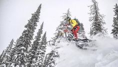 a person on a snow bike jumping in the air over some trees and snow covered ground