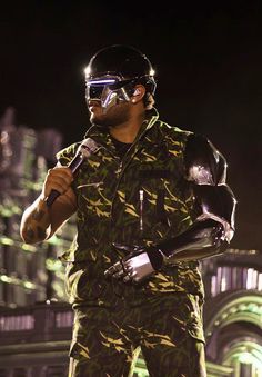 a man in camouflage holding a microphone and wearing goggles on top of his head