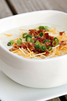 a bowl of soup with bacon, cheese and green onions on top sits on a plate