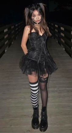 a woman in a black dress and striped stockings is standing on a wooden bridge at night