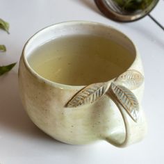 a white cup filled with green tea sitting on top of a table next to leaves