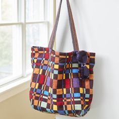 a multicolored handbag hanging from a hook on a wall next to a window