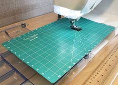 a green cutting mat sitting on top of a wooden floor next to a sewing machine