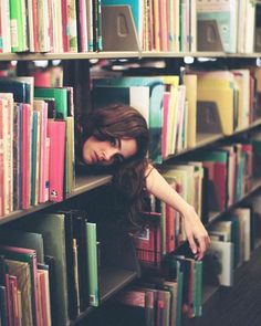 a woman leaning on a bookshelf with her head in the bookcases