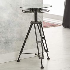 a glass table sitting on top of a metal stand in front of a white wall