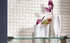 three white vases with purple flowers in them on a glass shelf against a tiled wall