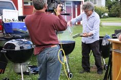 two men are cooking on the grills in front of their house while another man is filming them