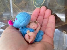 a hand holding a tiny blue stuffed animal in it's left palm, next to a glass bowl