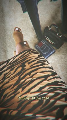 a person's foot is covered in black and brown zebra print, next to a purse