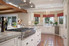 a large kitchen with white cabinets and marble counter tops, along with red tile flooring