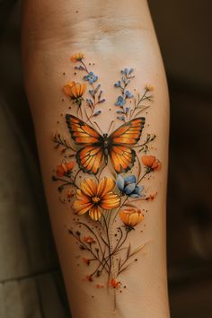 a woman's thigh with an orange butterfly and blue flowers tattoo on it,