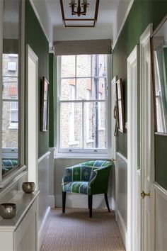 a green and white chair sitting in front of a window next to a mirror on the wall