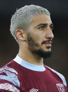 a man with grey hair and a goatee looks off to the side while wearing a maroon jersey