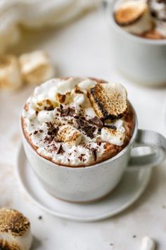 two cups of hot chocolate and marshmallows on a white table with cookies