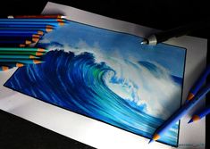 some colored pencils are next to a drawing of a wave