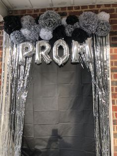 an arch decorated with silver and black balloons that say prom on the front, surrounded by pom poms