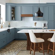 a kitchen with blue cabinets and white counter tops, two bar stools at the center