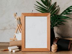 a wooden frame sitting on top of a table next to a potted plant and pencils