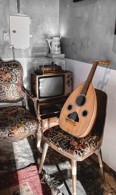 a guitar sitting on top of a wooden chair next to a tv and microwave oven