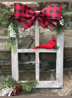 a red cardinal sitting on top of a window frame decorated with greenery and pine cones