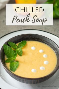 a bowl of peach soup on a plate with mint garnish and lemon wedges