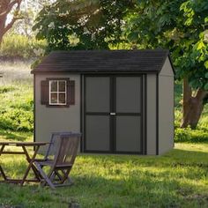 a small shed sitting in the grass next to a picnic table and two folding chairs