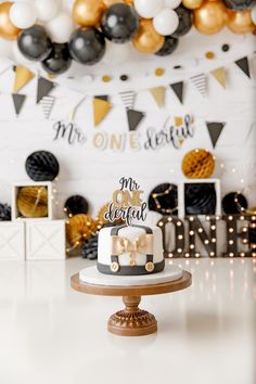 a cake sitting on top of a table in front of a wall with black and gold balloons