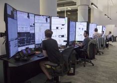 people sitting at desks with multiple screens on them