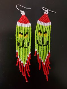 two green and red beaded earrings on a black surface, one with an angry face