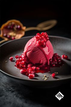 an ice cream sundae with pomegranates on a black plate next to a spoon