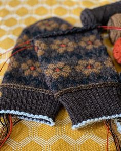 two knitted mittens sitting on top of a yellow and white cloth covered table