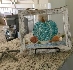 an old frame with sea glass and seashells in it on a kitchen counter