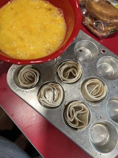 a red bowl filled with food next to muffin tins on top of a table