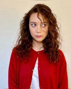 a young woman with curly hair wearing a red cardigan and white t - shirt