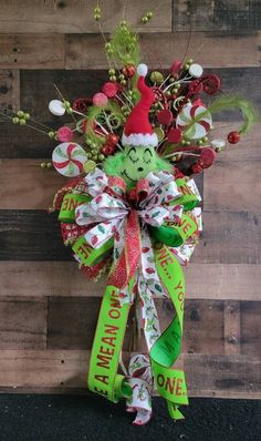 a christmas wreath with the grin face on it and green ribbon, hanging against a wooden wall