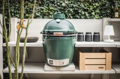 a large green grill sitting on top of a wooden table next to a plant and other items