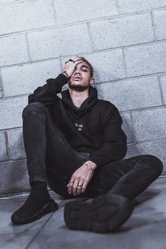 a man sitting on the ground in front of a brick wall with his hands to his face