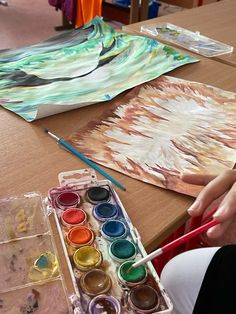 a person sitting at a table with some paint and watercolors in front of them