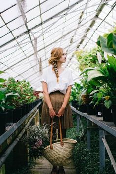 a woman standing in a greenhouse holding a basket