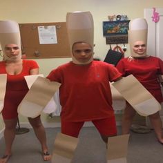 three people in red shirts and white paper hats are holding up large pieces of cardboard