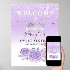 a person holding up a cell phone next to a welcome sign with purple roses on it