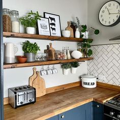 a kitchen with blue cabinets and wooden counter tops has a clock on the wall above it